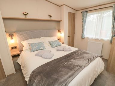 A bedroom with a bed made with white linens gray throw and blue floral pillows at 20 Wolds View in East Heslerton near West Heslerton