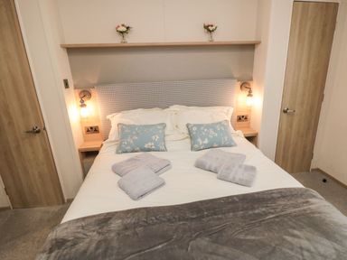 A bedroom with a double bed with floral pillows towels on bed two wooden doors on either side at 20 Wolds View East Heslerton near West Heslerton
