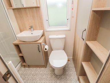 A bathroom with a toilet a sink with a cabinet a window and wooden shelves at 20 Wolds View in East Heslerton near West Heslerton
