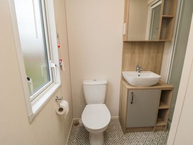 A bathroom with a toilet and a sink with storage cabinet and a window at 20 Wolds View East Heslerton near West Heslerton