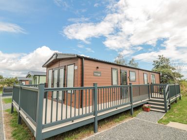A brown mobile home with a wraparound grey deck and stairs outside under a blue sky at 20 Wolds View in East Heslerton near West Heslerton