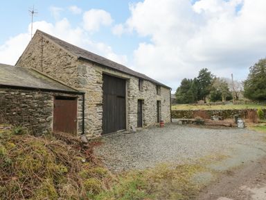 A stone barn with large wooden doors and a gravel driveway surrounded by trees at Myra's View in Newby Bridge