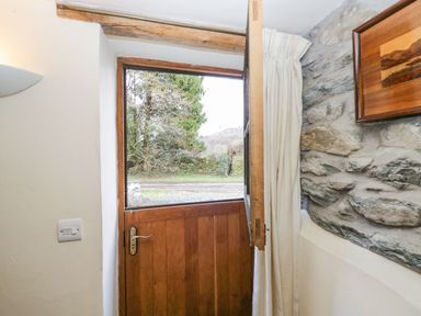A wooden stable door partially open with curtains and a stone wall inside a house at Myra's View in Newby Bridge