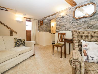 A sitting room with a beige sofa a wooden chair a plaid armchair with a sheep cushion stone walls and a wooden door at Myra's View in Newby Bridge