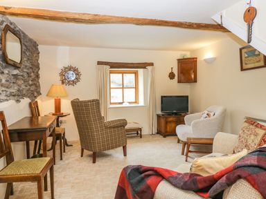 A sitting room with chairs a wooden table a television and a window at Myra's View in Newby Bridge