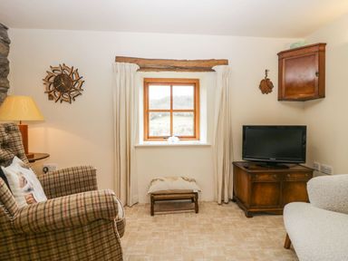 A living room with a window wooden cabinet tv armchair and footstool at Myra's View in Newby Bridge