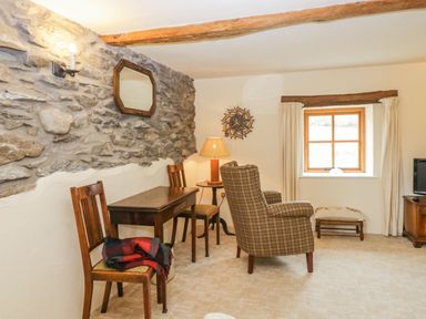 A room with stone and plaster walls wooden chairs a wooden table an armchair a window with curtains and a wall clock at Myra's View in Newby Bridge