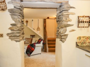 A view through a stone doorway into a living room with a couch with a plaid blanket and a staircase in the background at Myra's View in Newby Bridge