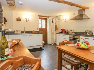 A kitchen with white cabinets a wooden table with fruit basket and utensils at Myra's View in Newby Bridge