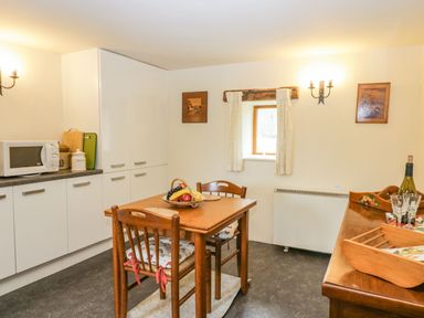 A kitchen with a wooden table and chairs a microwave and cabinets at Myra's View in Newby Bridge