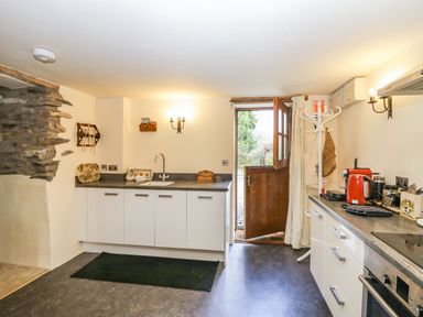 A kitchen with white cabinets a stone wall and a wooden door open to outside at Myra's View in Newby Bridge