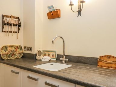 A kitchen countertop with a sink wooden spoons on a rack and decorative trays at Myra's View in Newby Bridge