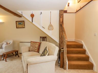A living room with a beige sofa and armchair near a staircase with striped carpet at Myra's View in Newby Bridge