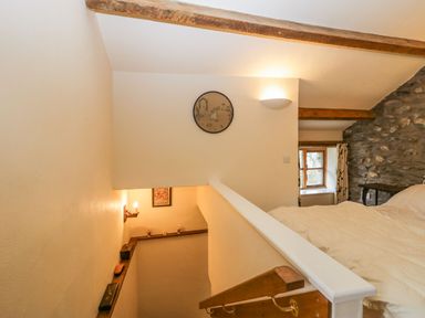 A bedroom with a bed near a stone wall window and a staircase with wooden handrail at Myra's View in Newby Bridge