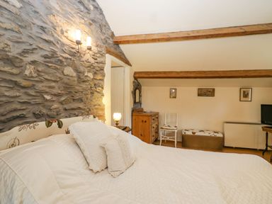 A bedroom with a bed white pillows wooden beams stone wall and furniture at Myra's View in Newby Bridge