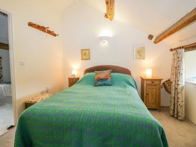A bedroom with a bed covered in a green and blue blanket two bedside tables with lamps and framed pictures on the wall at Myra's View in Newby Bridge