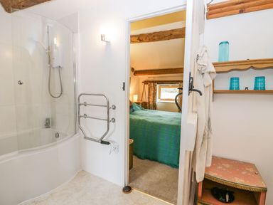 A bathroom with a bathtub and shower next to a bedroom with a bed covered with a green blanket at Myra's View in Newby Bridge