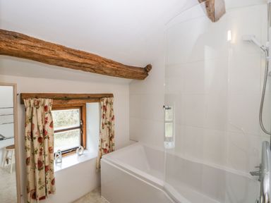 A bathroom with a bathtub and shower next to a window with floral curtains and wooden beams at Myra's View in Newby Bridge