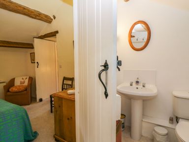 A bedroom with an armchair and wooden furniture next to a bathroom with a sink and toilet at Myra's View in Newby Bridge