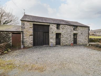 A stone barn with wooden doors and windows and a gravel driveway at Myra's View in Newby Bridge