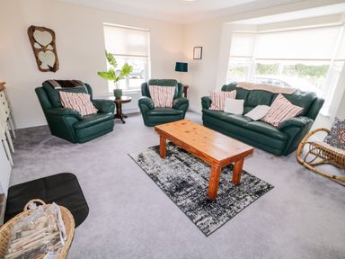 A living room with green leather sofa and armchairs with striped cushions a wooden coffee table on a rug and windows with blinds at The Glen in Carndonagh County Donegal