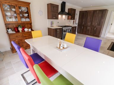 A kitchen with a white dining table and colorful chairs next to wooden cabinets and a hutch at The Glen in Carndonagh County Donegal
