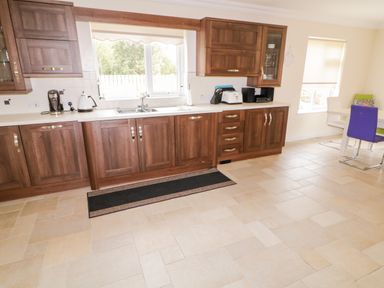 A kitchen with wooden cabinets a sink a coffee maker a kettle a toaster and a dining area with chairs at The Glen in Carndonagh County Donegal