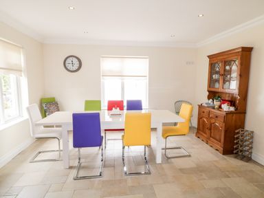 A dining room with a white table surrounded by multicolored chairs and a wooden cabinet at The Glen in Carndonagh County Donegal