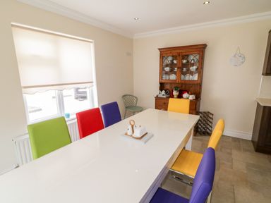 A dining room with a white table surrounded by colorful chairs and a wooden cabinet with dishes at The Glen in Carndonagh County Donegal