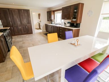 A kitchen with dark wood cabinets a white dining table and colorful chairs at The Glen in Carndonagh County Donegal