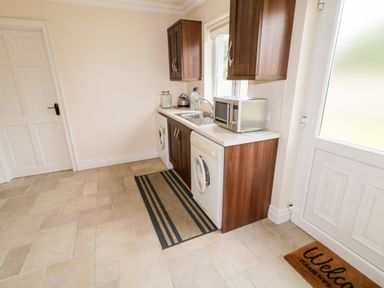 A utility room with washing machines a sink microwave wooden cabinets and a welcome mat on tiled floor at The Glen in Carndonagh County Donegal