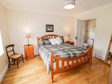 A bedroom with a wooden bed and nightstands with lamps a wooden chair and a door leading to a bathroom at The Glen in Carndonagh County Donegal