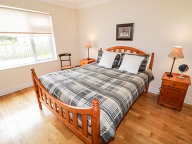 A bedroom with a wooden double bed with plaid bedding two bedside tables with lamps a small chair near the window at The Glen in Carndonagh County Donegal