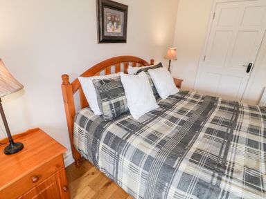 A bedroom with a wooden bed and checkered bedspread beside wooden nightstands with lamps at The Glen in Carndonagh County Donegal