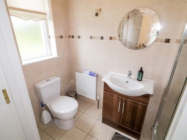 A bathroom with a toilet, sink with cabinet, round mirror, and window at The Glen in Carndonagh County Donegal