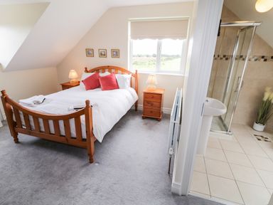 A bedroom with a wooden bed and bedside tables with lamps and an adjacent bathroom with a shower at The Glen in Carndonagh County Donegal