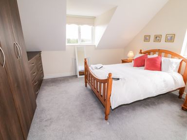 A bedroom with a wooden bed white bedding and red pillows a wardrobe a standing mirror and a lamp on a bedside table at The Glen in Carndonagh County Donegal