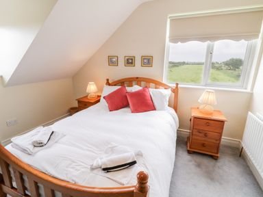A bedroom with a wooden bed white bedding two red pillows wooden nightstands with lamps and a window showing a grassy field at The Glen in Carndonagh County Donegal