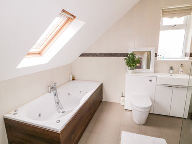 A bathroom with a bathtub under a skylight a toilet a sink with cabinets and a window at The Glen in Carndonagh County Donegal