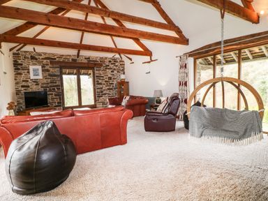 A living room with leather sofas a hanging chair and exposed wooden beams at Birchenhayes in St Dominick