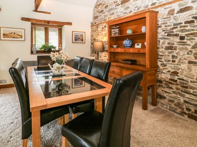 A dining room with a wooden and glass table black leather chairs a wooden cabinet with decorations and a stone wall at Birchenhayes in St Dominick