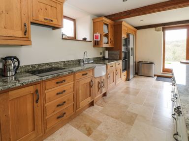 A kitchen with wooden cabinets stone countertops and tiled floor at Birchenhayes in St Dominick