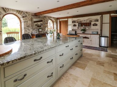 A kitchen with a large island counter with chairs and flowers on the counter at Birchenhayes in St Dominick