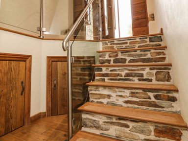 A staircase with stone and wood steps with glass and metal railing and wooden doors at Birchenhayes in St Dominick