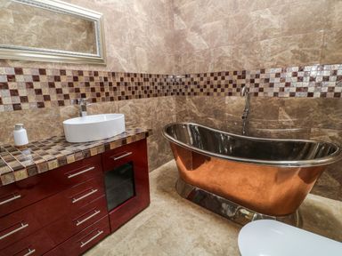 A bathroom with a copper bathtub a white sink on a tiled countertop and a mirror above at Birchenhayes in St Dominick