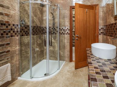 A bathroom with a glass shower enclosure a tiled countertop with a white sink and a wooden door at Birchenhayes in St Dominick