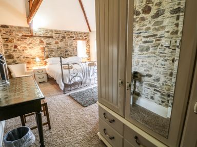A bedroom with a metal bed frame bedside tables lamps a wardrobe with a mirror and an armchair at Birchenhayes St Dominick