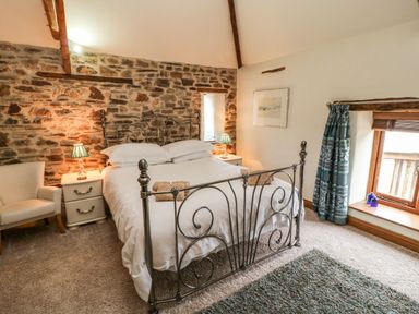 A bedroom with a metal bed frame and exposed stone wall at Birchenhayes in St Dominick