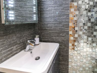 A bathroom sink with a faucet soap dispenser and a mirror with lights on a textured wall at Birchenhayes in St Dominick