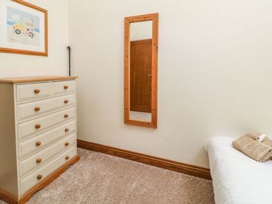 A bedroom corner with a chest of drawers a wall mirror and a bed with folded towels at Birchenhayes in St Dominick